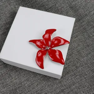 Close-up detail of a red enamel flower brooch on a white box, showcasing exquisite floral design.