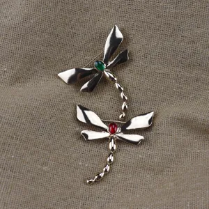 Close-up detail of vintage alloy dragonfly brooch with vibrant green and red enamel stones.
