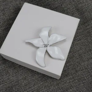 Detail of white enamel flower brooch, elegant floral clothing accessory for daily wear.