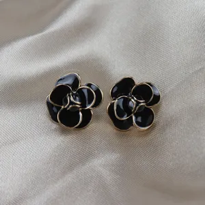 Close-up of black camellia enamel stud earrings with gold trim on satin background.