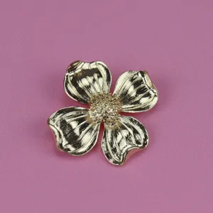 Close-up of vintage gold-toned four-petal flower brooch, textured metallic finish.