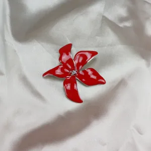 Red enamel iris brooch detail close up, shiny metallic flower pin for elegant outfit styling.