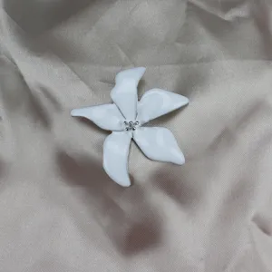 Close-up detail of a white enamel flower brooch with silver stamen beads on glossy satin background.