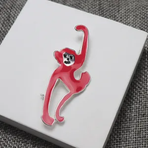 Dettaglio di una elegante spilla in smalto rosso a forma di scimmia su supporto bianco.