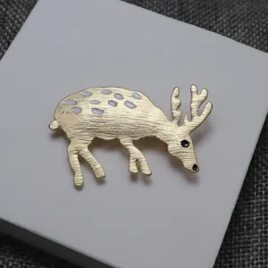 Elegante spilla a forma di cervo dorato con macchie di smalto bianco e dettagli unici.
