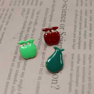 Dettaglio in primo piano di spille smaltate a forma di mela e pera con colori vivaci e bordi.