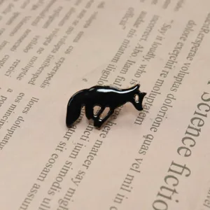 Close-up detail of a cute black running fox enamel brooch pin, set on vintage book page.