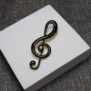 Music note enamel brooch close up, black and gold treble clef lapel pin accessory.