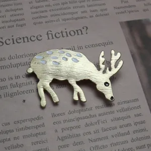 Spilla a forma di cervo dorato con macchie di smalto bianco, vista dettagliata dell'accessorio.