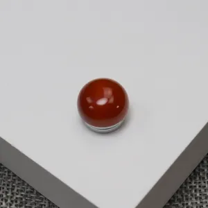Close up detail of round red agate magnetic brooch showing smooth surface texture and metal base.