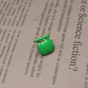 Primo piano dettagliato di una simpatica spilla smaltata a forma di mela verde con bordo oro.