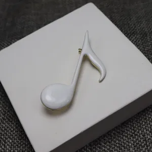 White enamel musical note brooch detail shot, showing exquisite gold-trimmed craftsmanship.
