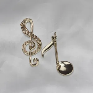 Close-up detail of gold-tone music note brooch backs, showing pin mechanism and texture.