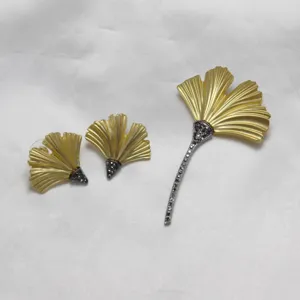 Detailed view of matte gold ginkgo leaf brooch and earrings set with black rhinestones.