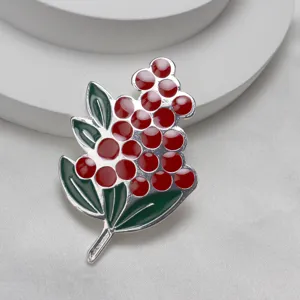 Primo piano dettaglio della spilla smalto bacche rosse con foglie verdi, accessorio metallo.
