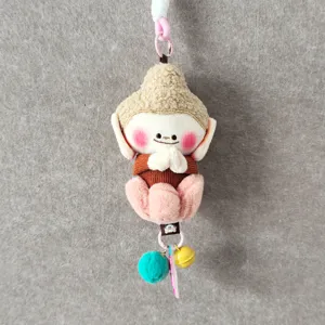 Close-up view of cute cultural plush pendant with monk design, prayer hands and small charms.