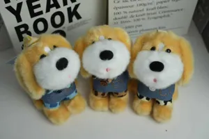 Simatico ciondolo giocattolo cane in peluche, bambola animale giallo bianco con salopette jeans.