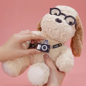 Close-up detail of cute plush puppy toy wearing black round glasses and mini camera pendant.