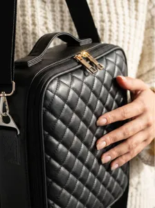 Close-up of black quilted leather cosmetic bag with gold zippers and stylish top handle.