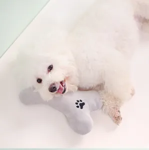 Close-up detail of a cute puppy resting on a soft grey bone-shaped plush pet toy.