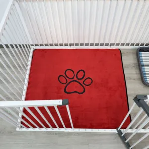 Red washable pet pee pad with black paw print design placed inside white safety playpen gate.