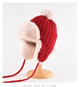 Red knitted trapper hat detail showing beige faux fur lining, pom-pom, and warm ear flaps.
