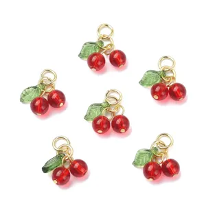 Detailed shot of red cherry glass charms with green leaves and gold jump rings for DIY crafts.
