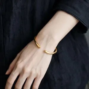 Vista di dettaglio di un bracciale rigido dorato, gioiello da polso a goccia minimal.