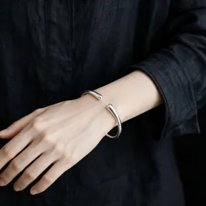 Primo piano del dettaglio del bracciale rigido aperto in argento minimalista sul polso.