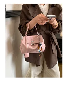 Detail shot of stylish pink suede handbag with metal lock and bead charm, elegant daily wear.