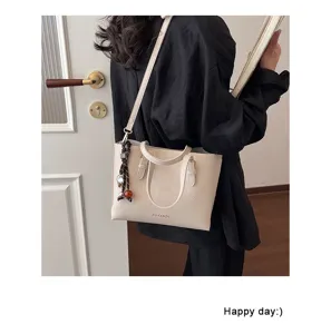 Vista detallada del bolso tote texturizado beige con asas dobles y bonito colgante.