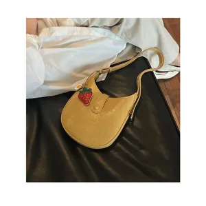 Detail view of the yellow leather saddle shoulder bag with a cute strawberry pendant detail.
