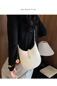 Detailed shot of the chic cream leather underarm saddle bag with cute strawberry charm.