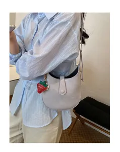 Chic minimalist saddle bag detail, light gray leather texture with cute strawberry charm.