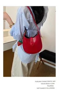 Red leather saddle bag for women, stylish underarm shoulder bag with strawberry charm.