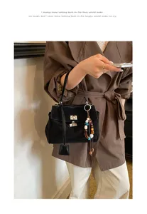 Black suede women handbag with metal lock and colorful beaded charm, minimalist detail shot.