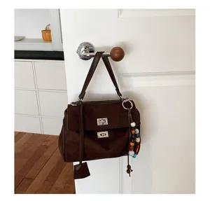 Brown suede handbag detail, featuring metallic turn-lock closure and decorative beaded charm.