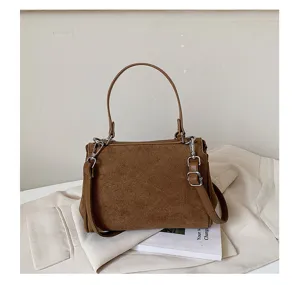 Close-up of brown suede handbag detail, featuring metallic rings and soft texture.