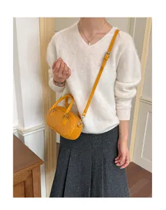 Detail shot of a stylish yellow woven handbag worn with a white sweater and grey skirt.