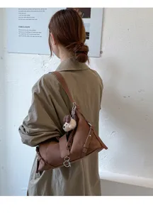 Retro braune Schultertasche unter dem Arm mit niedlichem Plueschhund Anhänger Detail.