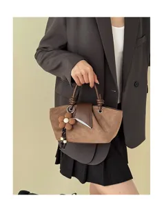 Brown suede handbag detail showcasing elegant flower charm and unique flap closure design.