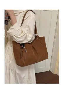 Close-up of brown leather shoulder bag with zipper pocket, chic tassels and metal ring detail.