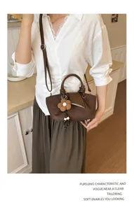 Detail view of the brown suede handbag featuring a cute flower charm and elegant handle.