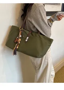 Detail view of green canvas shoulder tote bag with tassel pendant and metal turn lock.