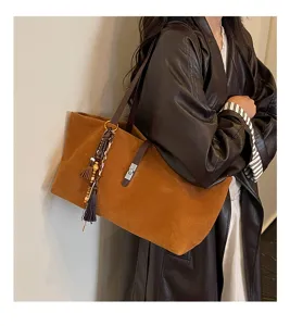 Vista detallada de un bolso tote de ante marrón vintage con borla elegante y cierre metálico.