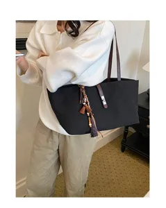 Casual black canvas tote bag with brown straps and elegant bohemian tassel charms.