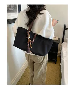Detailed view of the black canvas tote bag worn on shoulder, featuring chic tassel pendant.
