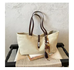 Detailed view of beige canvas tote bag featuring brown leather handles and chic tassel charm.