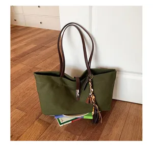 Detail shot of retro green canvas tote bag featuring brown leather handles and chic beaded tassel.