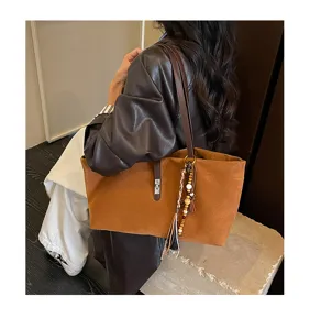 Detalle de un bolso tote retro de ante marrón con borla de cuentas y hebilla metálica.